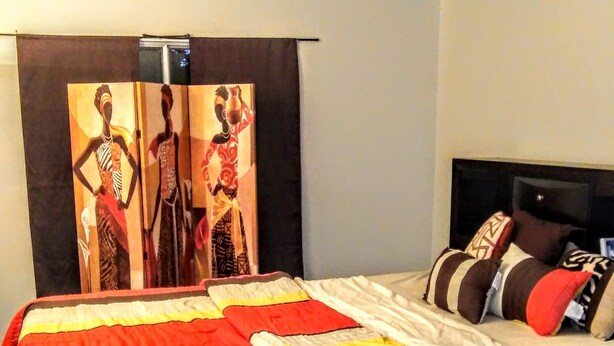 Uma cama com colcha colorida, cabeceira e parede com um quadro.