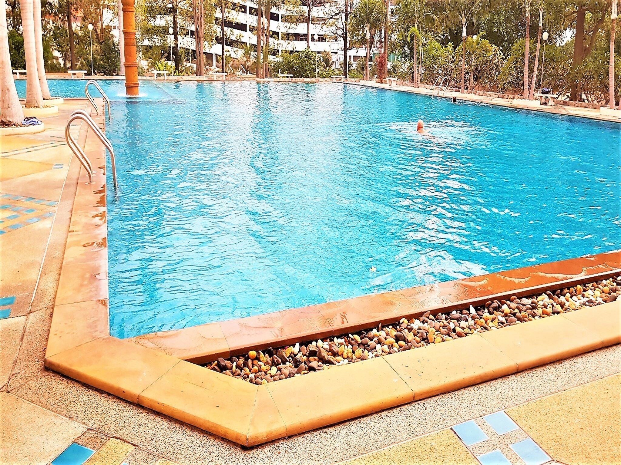 A swimming pool with clear blue water, surrounded by a tiled deck and a pebble border.