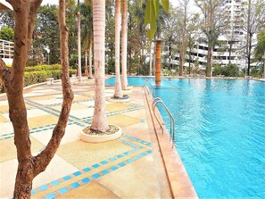 A swimming pool with a tiled deck and palm trees. - View Talay 5 Studio Apartment - Close to the Beach (Pattaya)