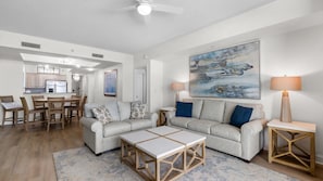 A modern living room with a grey sofa, a coffee table, and a dining area with wooden chairs and a table. - $150 activities - E-gift card when you book - Beautiful Oceanfront | Indoor/Outdoor Pools | NBP1916 (North Myrtle Beach)