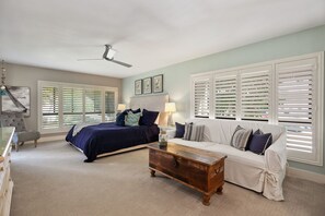 A bedroom with a bed, a white sofa, a wooden chest, and a ceiling fan.