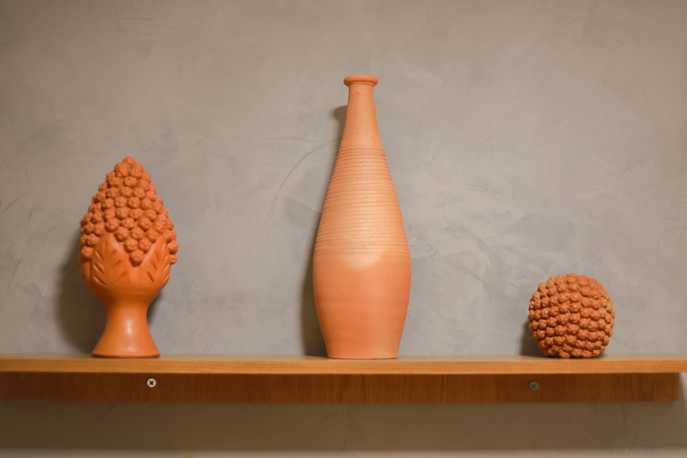 Tres jarrones de cerámica sobre una repisa de madera frente a una pared lisa.