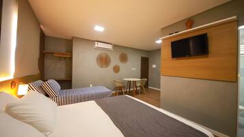 A hotel room with a bed, bedside table, lamp, wall-mounted TV, and a small dining area with chairs and a table.