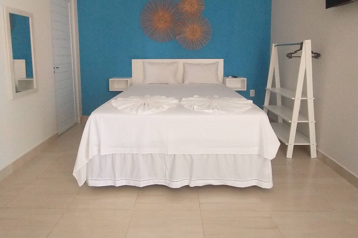 Ein Schlafzimmer mit einem Bett, einer blauen Akzentwand, einem weißen Kopfteil, einem weißen Nachttisch, einer weißen Kommode, einer weißen Leiter und einem an der Wand montierten Flachbildfernseher.