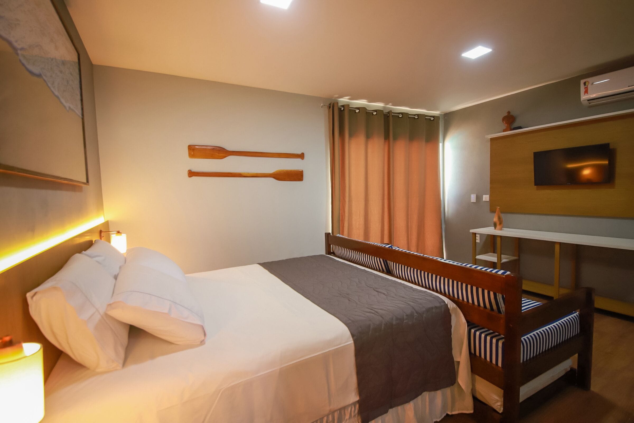 A hotel room with a bed, a wooden headboard, a TV on the wall, and a window with curtains.