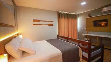 A hotel room with a bed, a wooden headboard, a TV on the wall, and a window with curtains.