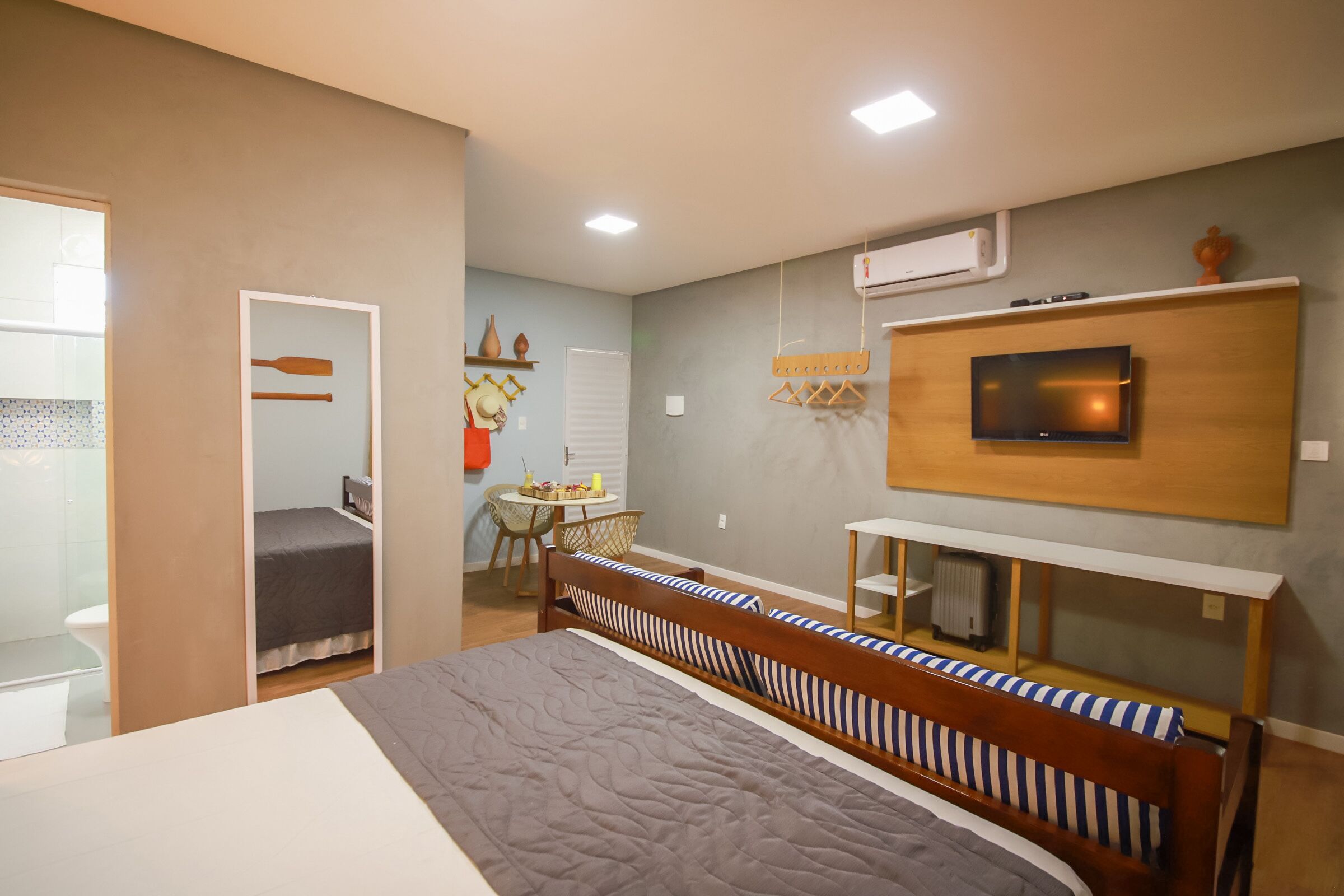 A modern bedroom with a large bed, a TV mounted on the wall, and a small desk area.