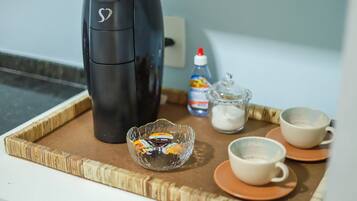 Uma bandeja com uma cafeteira, uma tigela de vidro com acompanhamentos e duas xícaras sobre uma mesa.