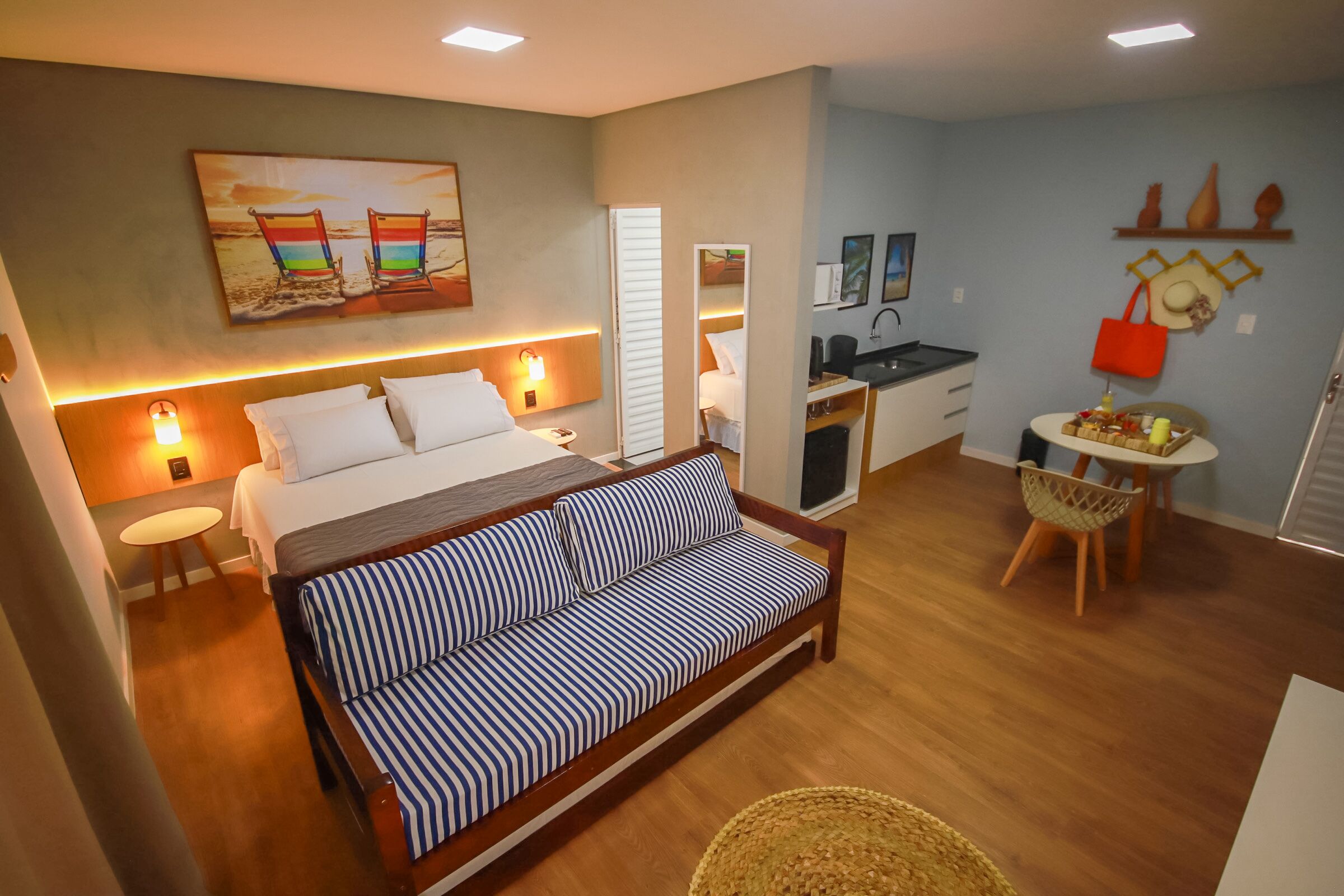 Habitación de hotel con cama, sofá, una mesita, una silla, zona de cocina y baño.