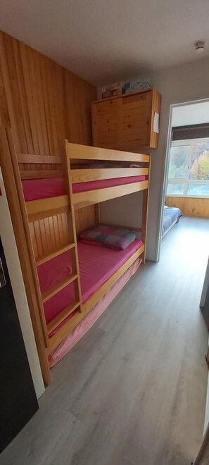 Quarto com beliches, paredes de madeira e janela.