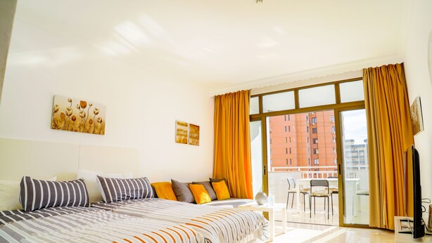 A modern hotel room with a large bed, a balcony with orange curtains, and a view of buildings. - VIP Studio at Hotel Las Palmeras (Fuengirola)