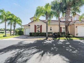 Una casa residencial con garaje, entrada para coches y palmeras.