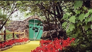 Un sentiero conduce a una porta verde circondata da fiori rossi e un recinto in legno.