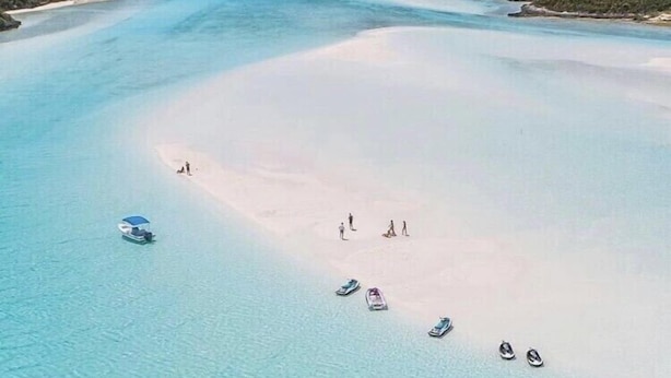 Vista aérea de uma praia com águas turquesas cristalinas, areal arenoso e vários barcos.