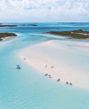 An aerial view of a beach with clear turquoise waters, a sandy shore, and several boats. - 
BEAUTIFUL BEACH HOUSE ON  TAR BAY  HEATED POOL ,  BAR & GRILL (Exuma)