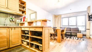 Eine moderne Küche mit Holzschränken, ein Essbereich mit einer Couch und große Fenster, die für natürliches Licht sorgen.