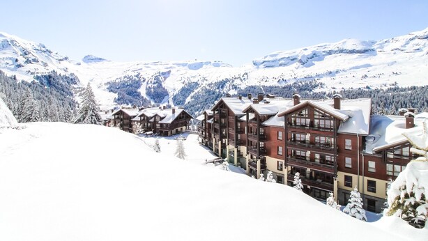 Ein schneebedecktes Bergresort mit Chalets, einer Skipiste und blauem Himmel.