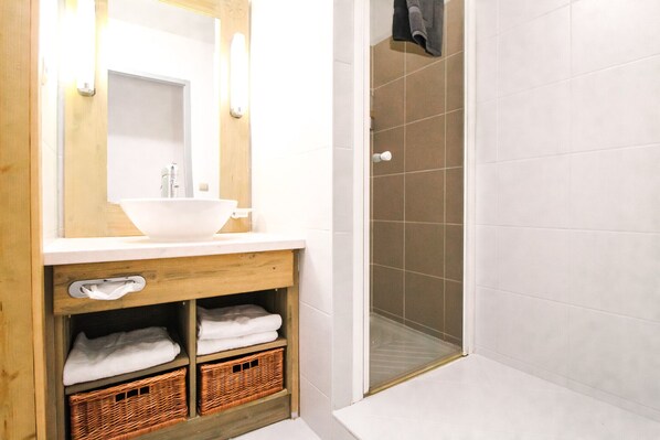 Un baño con tocador de madera, lavamanos blanco y cabina de ducha de vidrio.