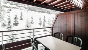 Ein Holzinnenraum mit Tisch und Stühlen, Blick auf verschneite Bäume und Berge.