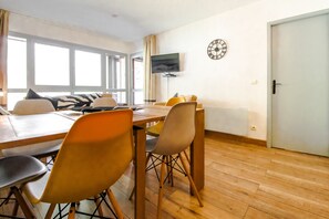 A dining area with a wooden table and chairs, a television on the wall, and a clock.