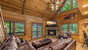 A log cabin interior with a stone fireplace, leather couches, and a television. - Highland Nook - Pet Friendly | Mountain View | Hot Tub | 3 Kings | Finnish Sauna (Morganton)