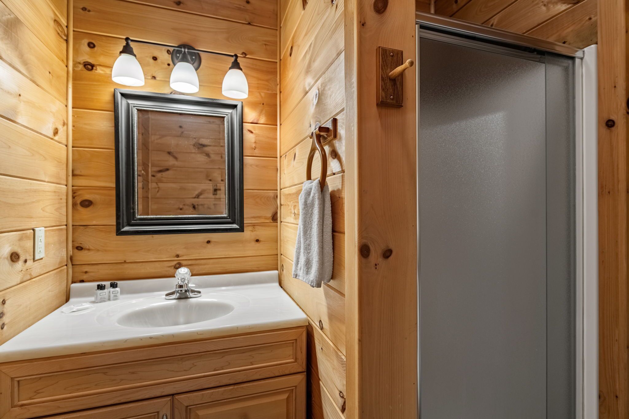 A wooden cabin bathroom with a white sink, two wall-mounted lights, and a framed mirror.