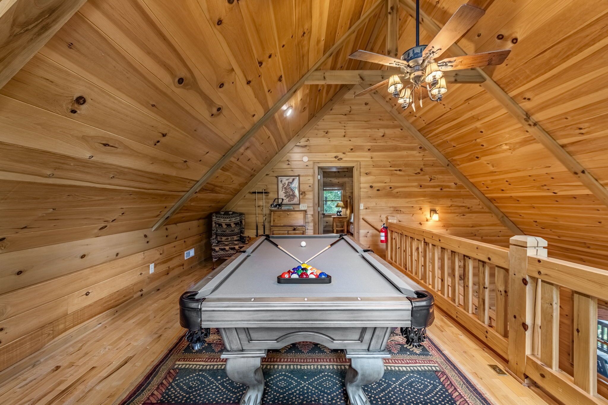 A pool table in a wooden room with a sloped ceiling and a ceiling fan.