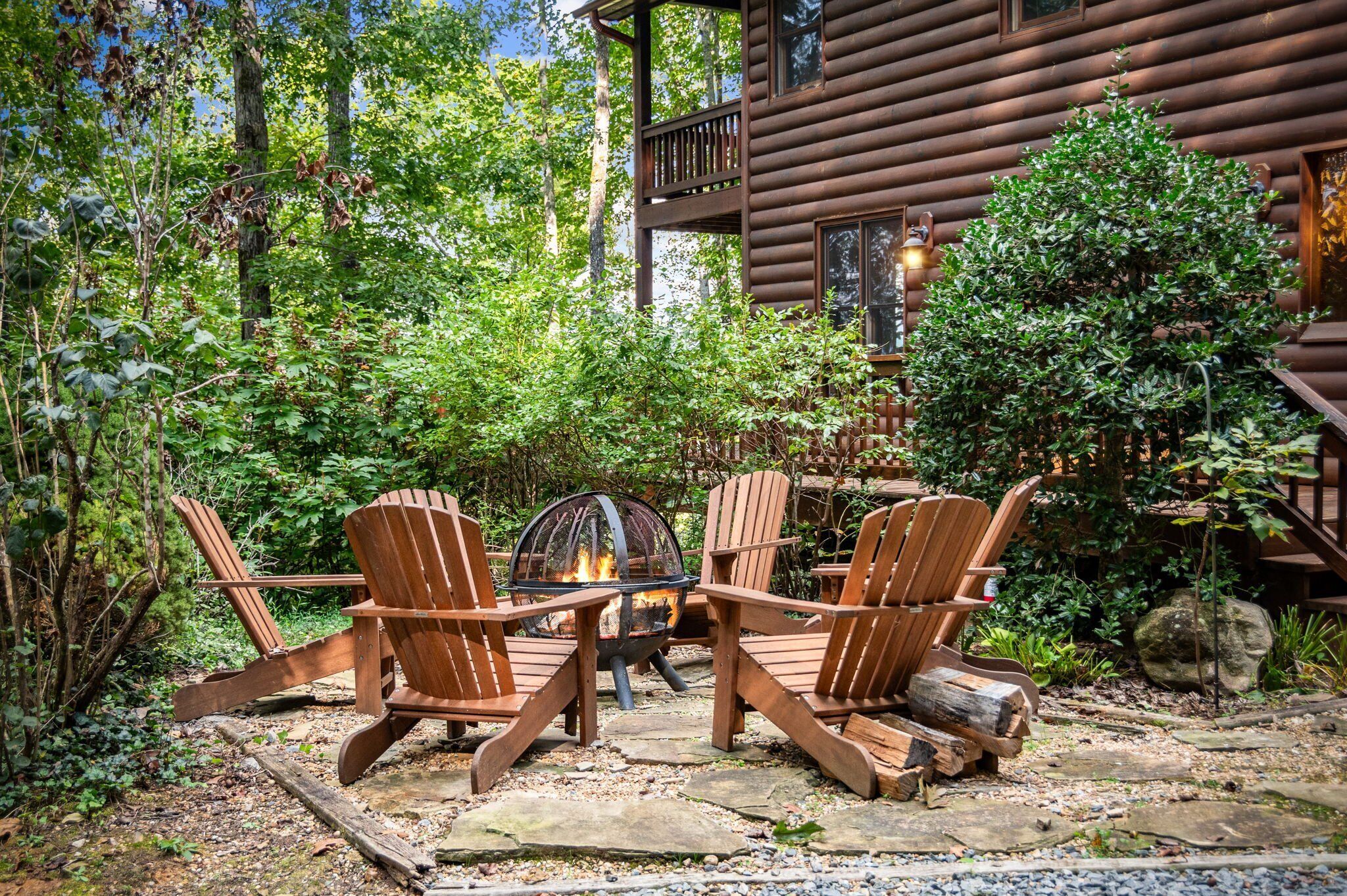 Uma cabana de troncos com uma fogueira e cadeiras Adirondack em uma área arborizada.