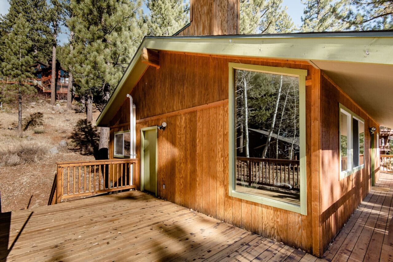 Une cabane en bois dotée d’une terrasse, de grandes fenêtres et d’une porte.