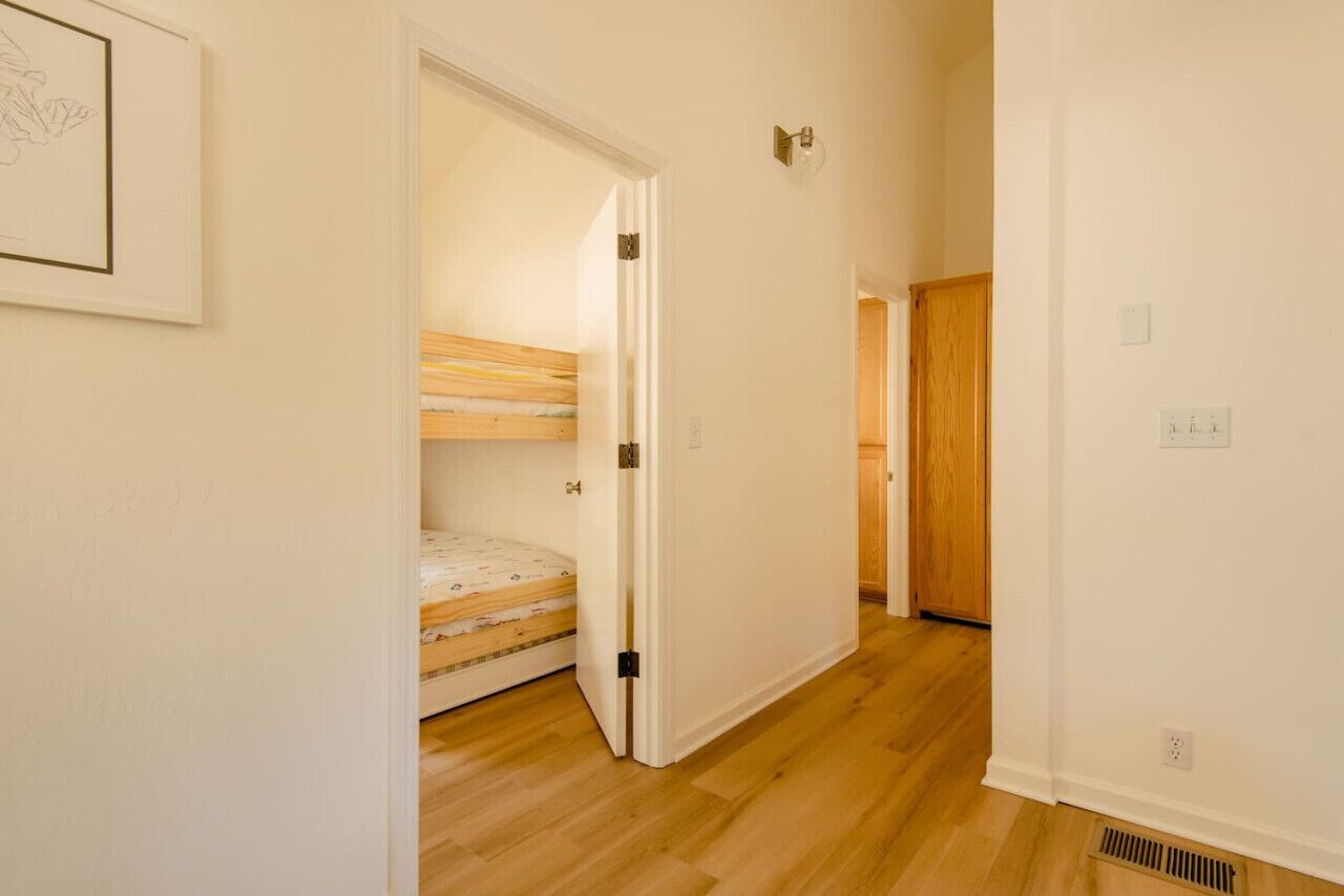 A hallway with a wooden floor, a bunk bed, and a door leading to another room.