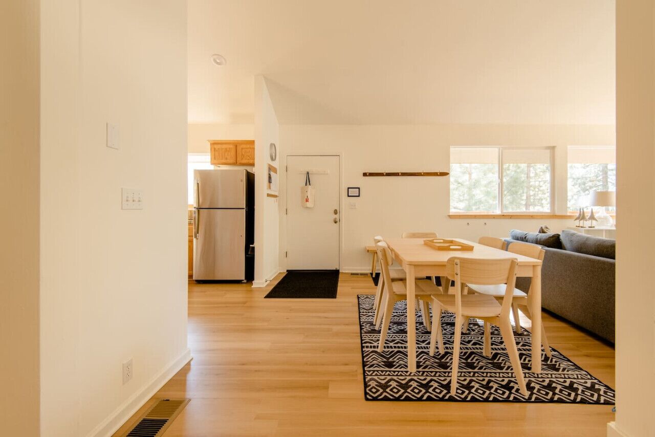 A modern kitchen with a refrigerator, a dining table with chairs, and a patterned rug.