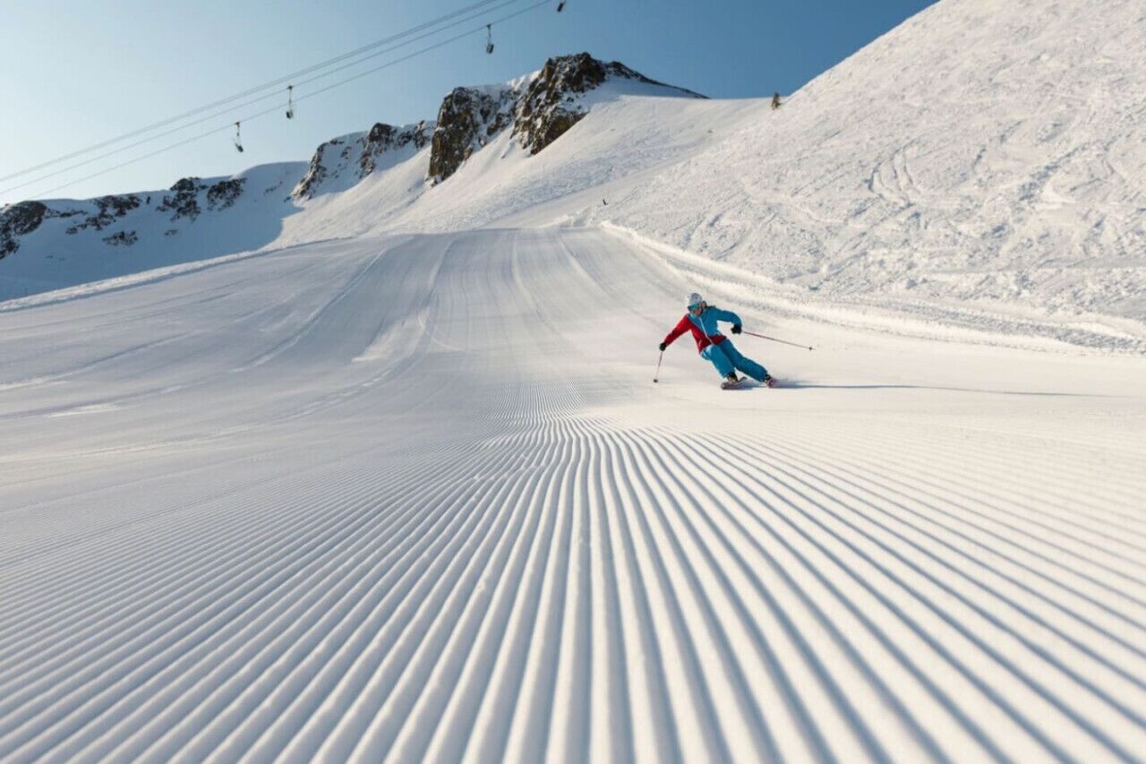 A ski slope with a skier in motion, ski lift cables, and a clear sky.