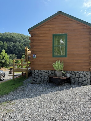 A wooden cabin with a stone foundation, a wooden deck, and a potted plant.