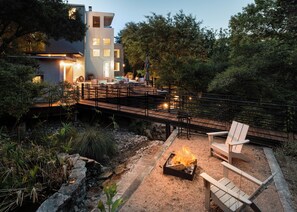 A modern outdoor deck with seating, a fire pit, and a view of a contemporary house. - Wild Basin: 10-15min to Austin · Heated Pool · SportCourt · Pickleball · Views (Austin)