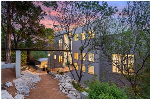 Uma casa moderna com área externa coberta, trilha de terra e árvores ao redor.