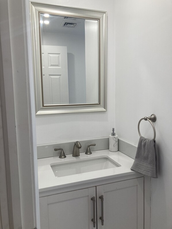 Un baño con un lavamanos blanco, tres grifos, un espejo con marco decorativo, un perchero para toallas y un armario con dos puertas.