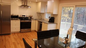 A modern kitchen with stainless steel appliances, a glass dining table, and a view of the outdoors. - Home w/game room hot tub 65" TV sauna AC (Albrightsville)