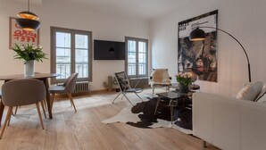 Un salon moderne comprenant un coin repas, de grandes fenêtres, un téléviseur fixé au mur et une affiche décorative.