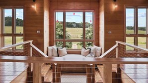 Un intérieur en bois avec un banc et une rambarde, de grandes fenêtres et une vue sur un paysage verdoyant.