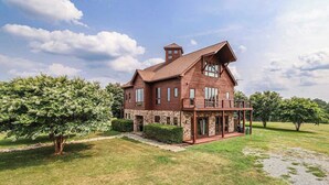 Une maison à deux étages, avec des fondations en pierre, un revêtement extérieur en bois et une grande véranda à l’avant.