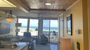 Ett rymligt vardagsrum med utsikt över stranden, träpanel i taket och en matplats med utsikt.