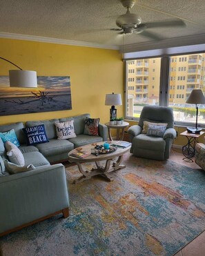 A living room with a sofa, armchair, coffee table, and a painting on the wall.