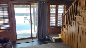 A spacious living room with a large window, a wooden staircase, and a plaid sofa. - Lake home pontoon included.  (Clear Lake)