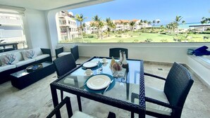 Varanda com mesa de vidro posta para refeições, com vista para um campo de golfe e edifícios.