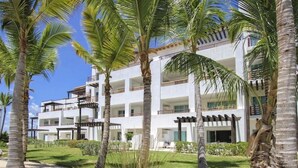 Um hotel com vários andares e varandas, rodeado por palmeiras e um jardim bem cuidado.