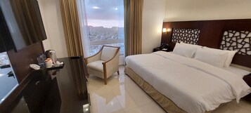 Habitación de hotel con una cama grande, un escritorio con teléfono, una silla y vistas a la ciudad a través de un ventanal amplio.