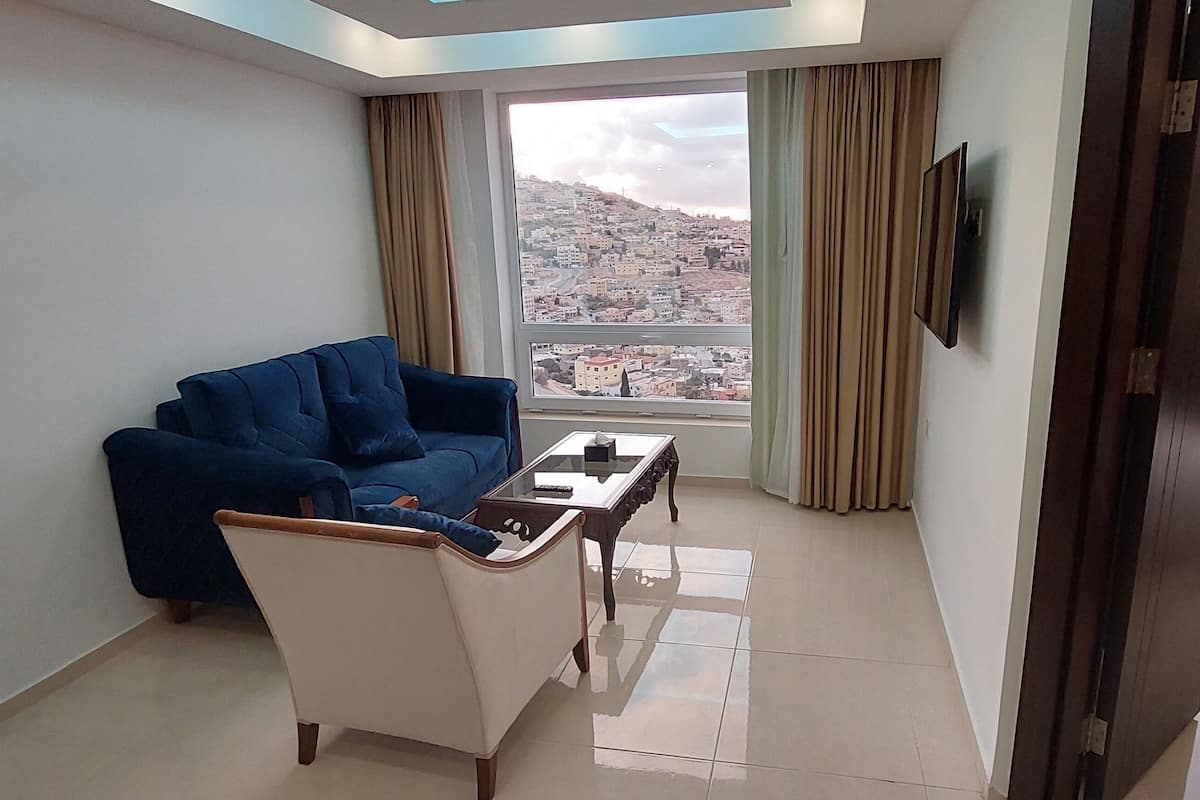 A hotel room with a bed, a sofa, a small table, a TV, and a window with a city view.