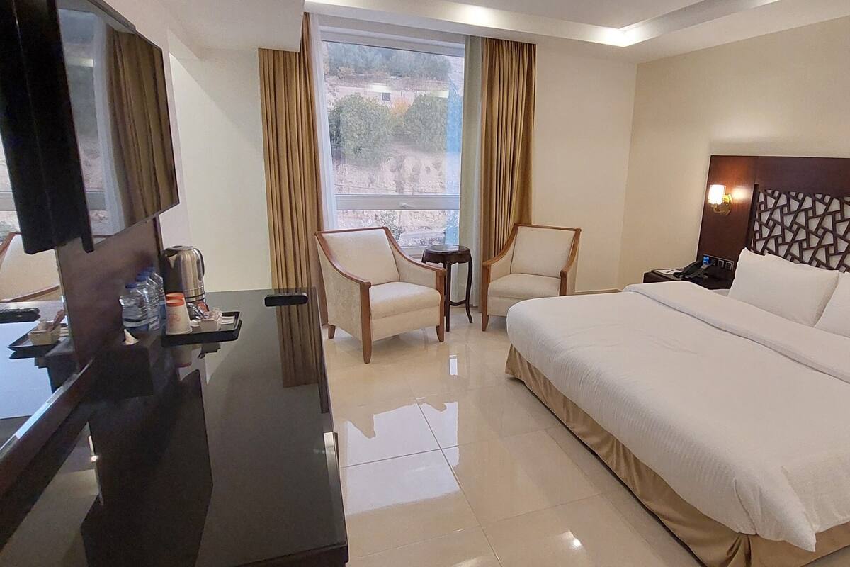 A hotel room with a large bed, a desk with a chair, a TV, and a window with curtains.