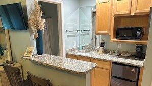 A compact kitchen with granite countertops, a built-in microwave, a refrigerator, and wooden cabinets.