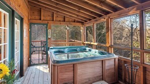 A wooden cabin with a hot tub, large windows, and a deck.